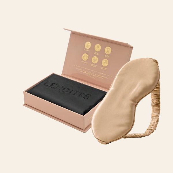 Pillowcase and Sleep Mask in Mulberry Silk by Lenoites featuring a beige silk sleep mask and a black mulberry silk pillowcase presented in an open blush pink box against a soft light background.