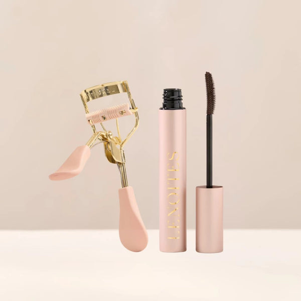 Love at First Lash by Lenoites featuring a pink eyelash curler with gold details and a rosegold PowerLash Growth Serum Mascara tube with a brown shade of the mascara, displayed against a soft beige background.