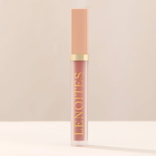 Tinted Lip Oil in Sophisticated by Lenoites, featuring a sleek tube with a pink cap and clear body, showcasing the blush tint, displayed against a soft beige background.