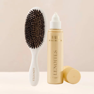 The Hair Growth Duo by Lenoites featuring a white hairbrush and the Hair Growth Serum in a transparent bottle with a golden tone, styled against a soft light beige background.