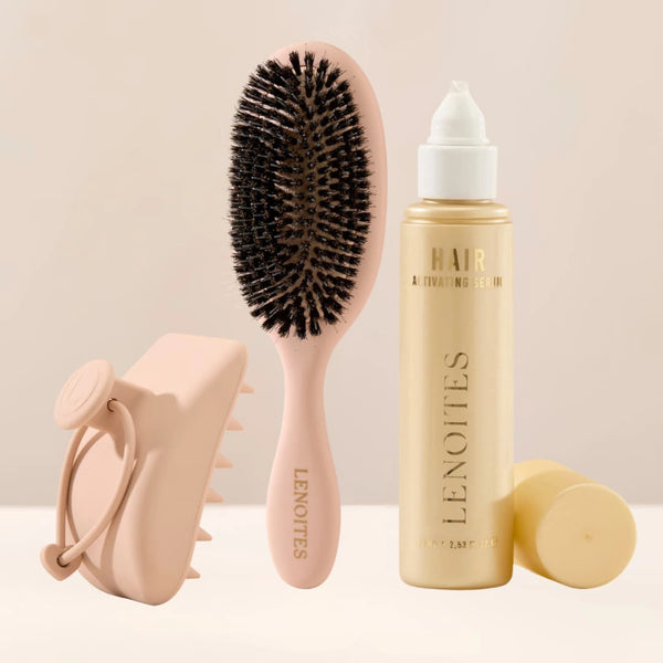 The Complete Hair Kit by Lenoites featuring a light pink hairbrush, a Hair Scalp Massager and the Hair Growth Serum in a transparent bottle with a golden tone, styled against a soft light beige background.