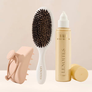 The Complete Hair Kit by Lenoites featuring a white hairbrush, a Hair Scalp Massager and the Hair Growth Serum in a transparent bottle with a golden tone, styled against a soft light beige background.
